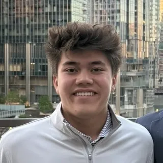 Amel Uzicanin smiling in an Illinois quarter-zip with city buildings behind