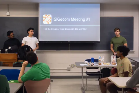 Two SIGecom members introducing "SIGecom Meeting #1" in front of the title slide
