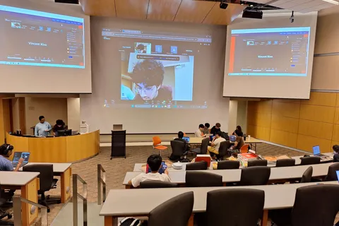 SIGecom members presenting over a video call to a full lecture hall audience